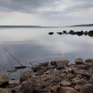 photo of rocky shoreline of a lake with a moody sky of clouds